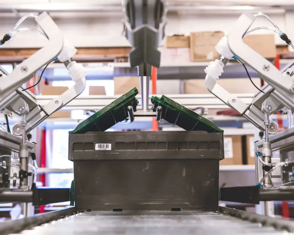 HS lid opener lifting the lid of a black tote on a conveyor